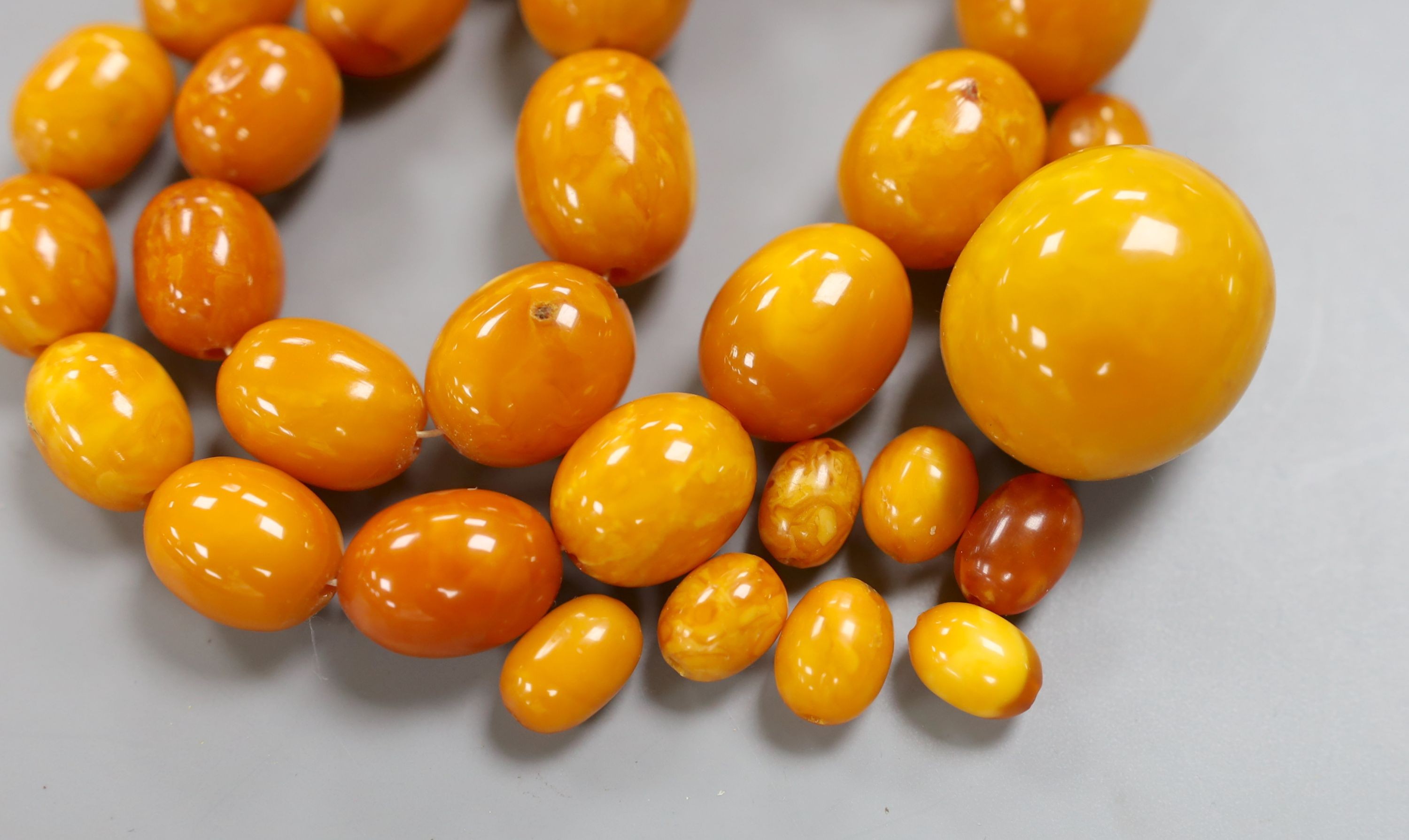 A single strand graduated oval amber bead necklace, 43cm, gross weight 51 grams and a few loose amber beads, 16 grams.